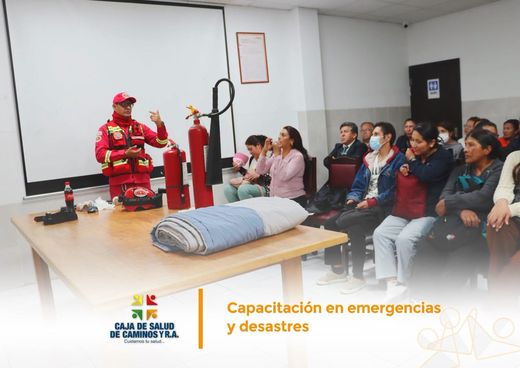 Un bombero con equipo rojo explica el uso de los extintores y una manta ignífuga al personal sentado en una sala.